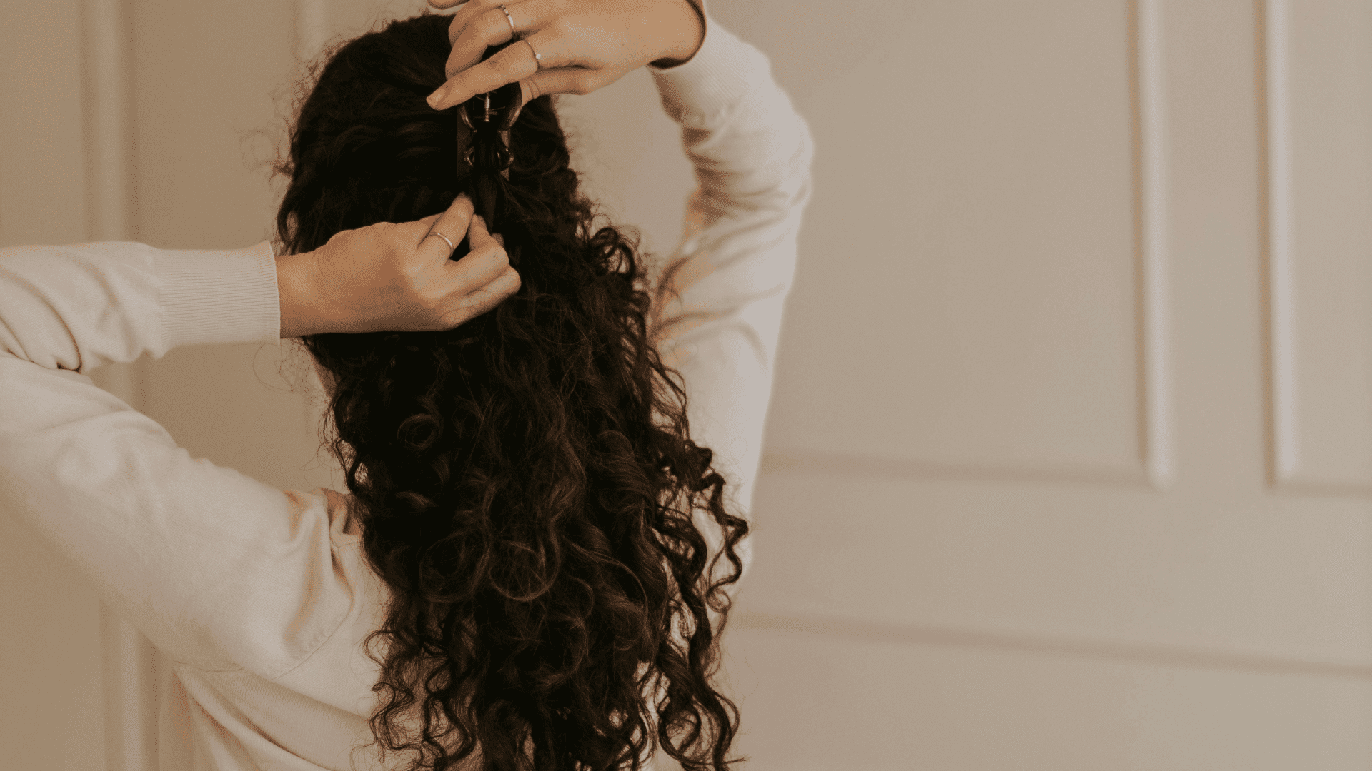 Woman styling long curly hair with a clip in a white room.