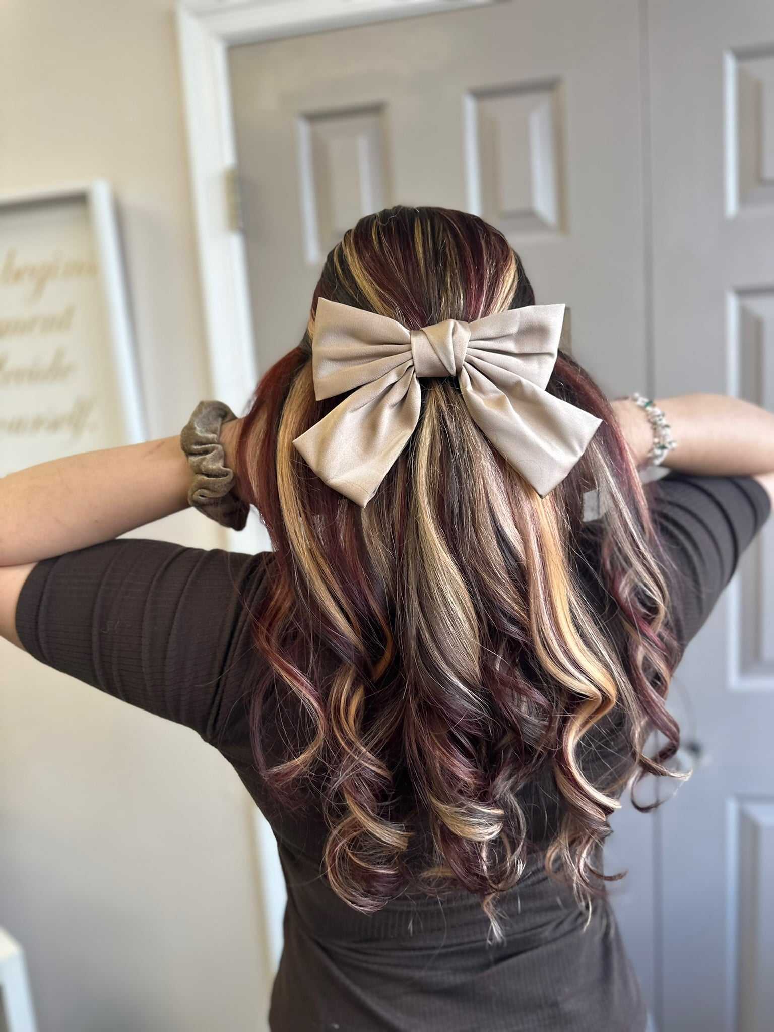 Hair with wavy blonde and brown highlights, styled with a large beige bow.