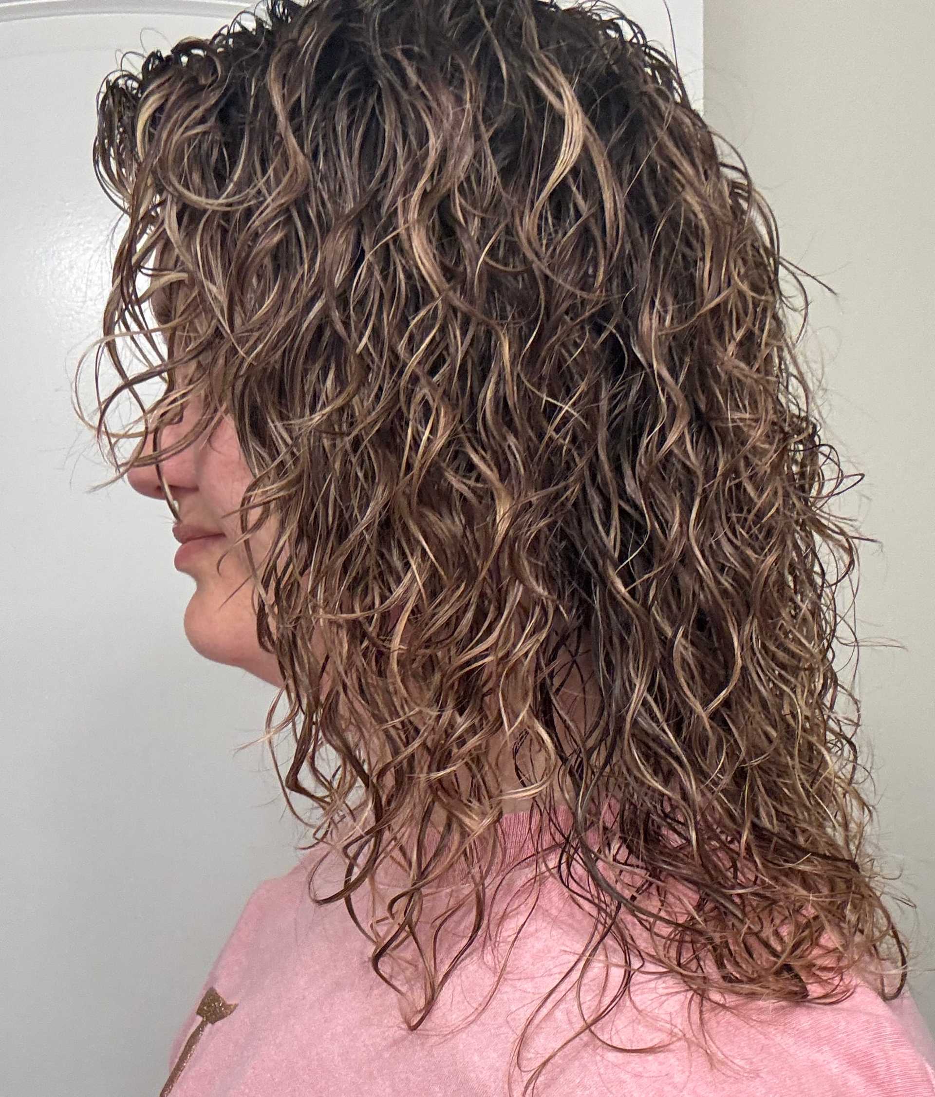 Curly-haired person in a pink shirt, side profile against a neutral background.