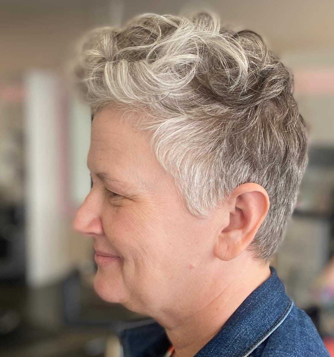 Short-haired person in profile wearing a denim jacket, smiling softly.