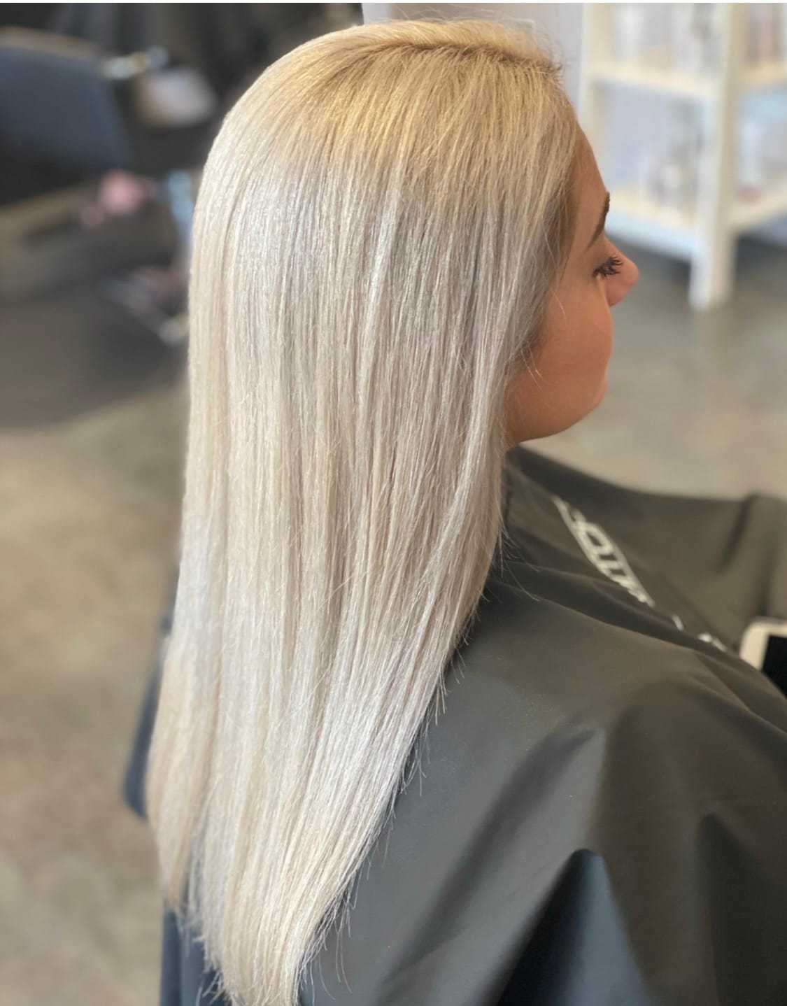 Blonde woman with straight hair getting styled at a salon, seated in a black chair.
