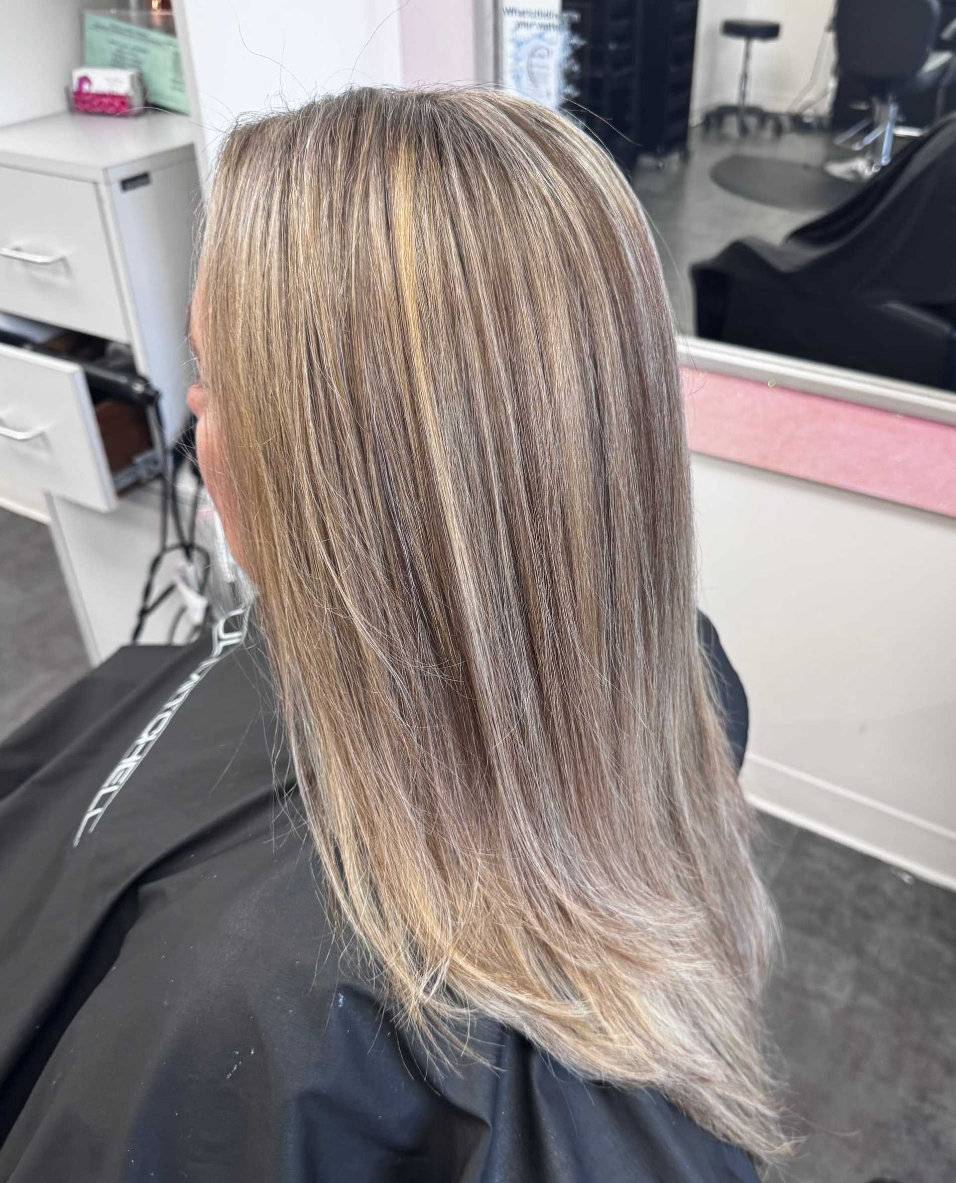 Blonde hair with highlights in a salon chair, mirror and styling area visible.