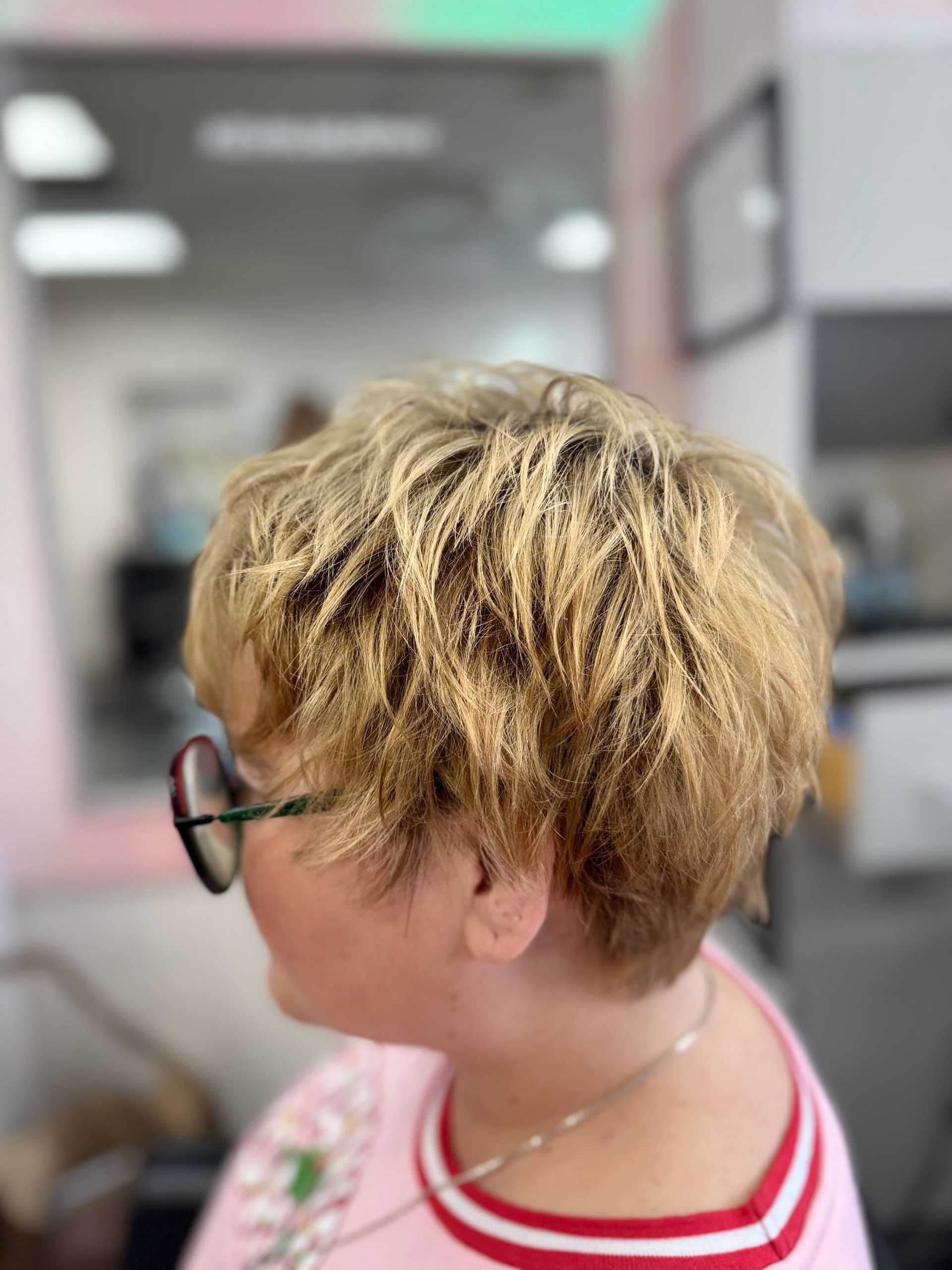 Short blonde hairstyle on a person wearing glasses, side view in a salon setting.