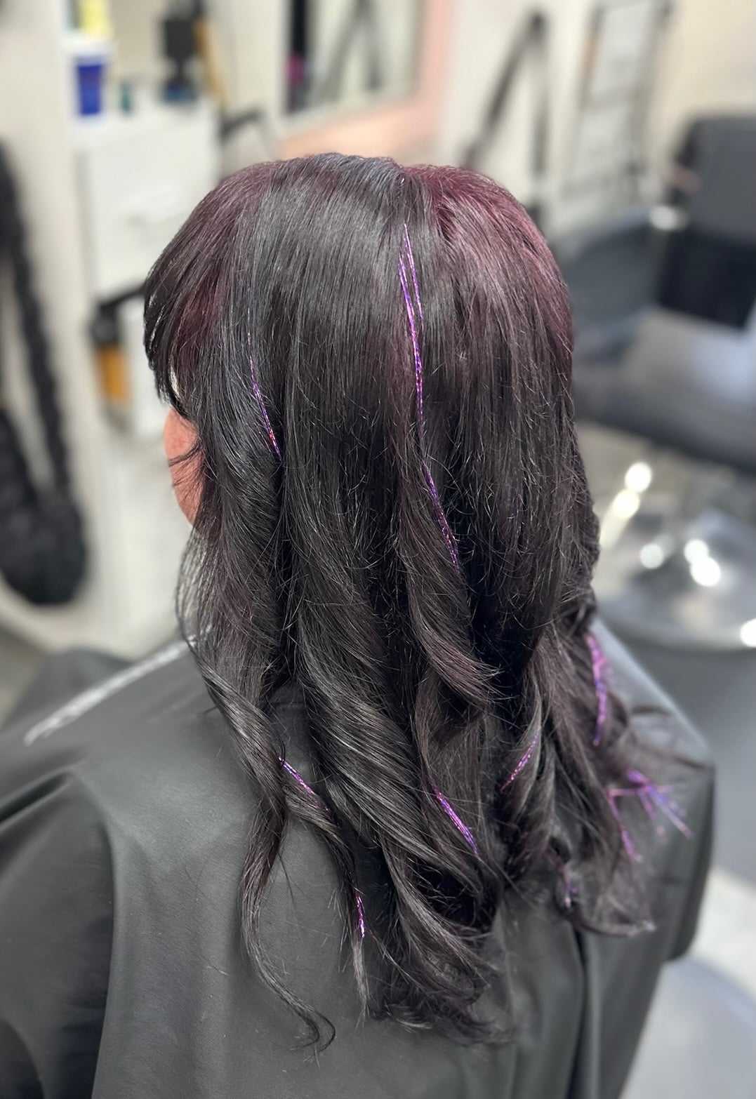 Woman with dark hair and purple highlights styled in curls at a salon.