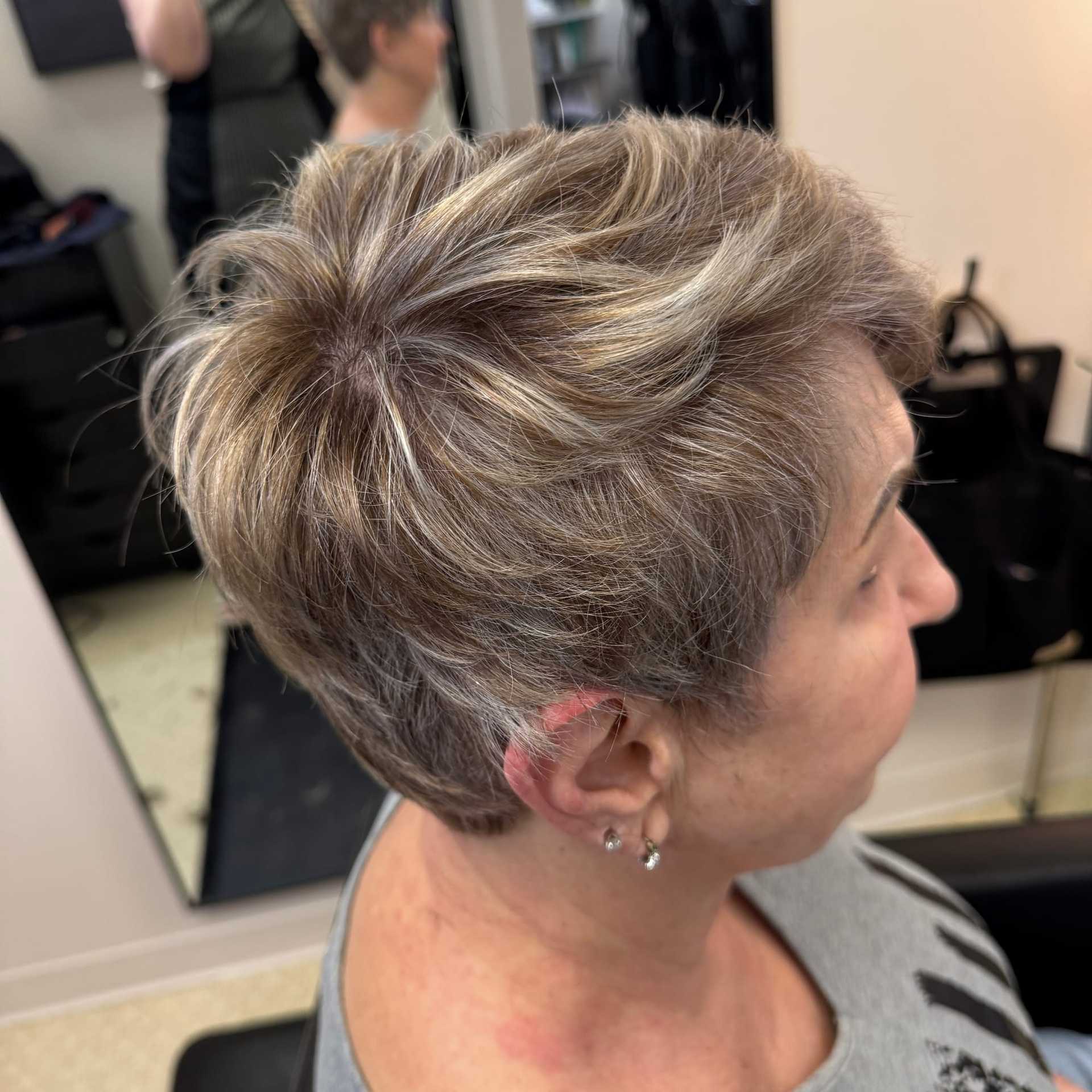 Short-haired woman in salon chair, side profile with mirror reflection.