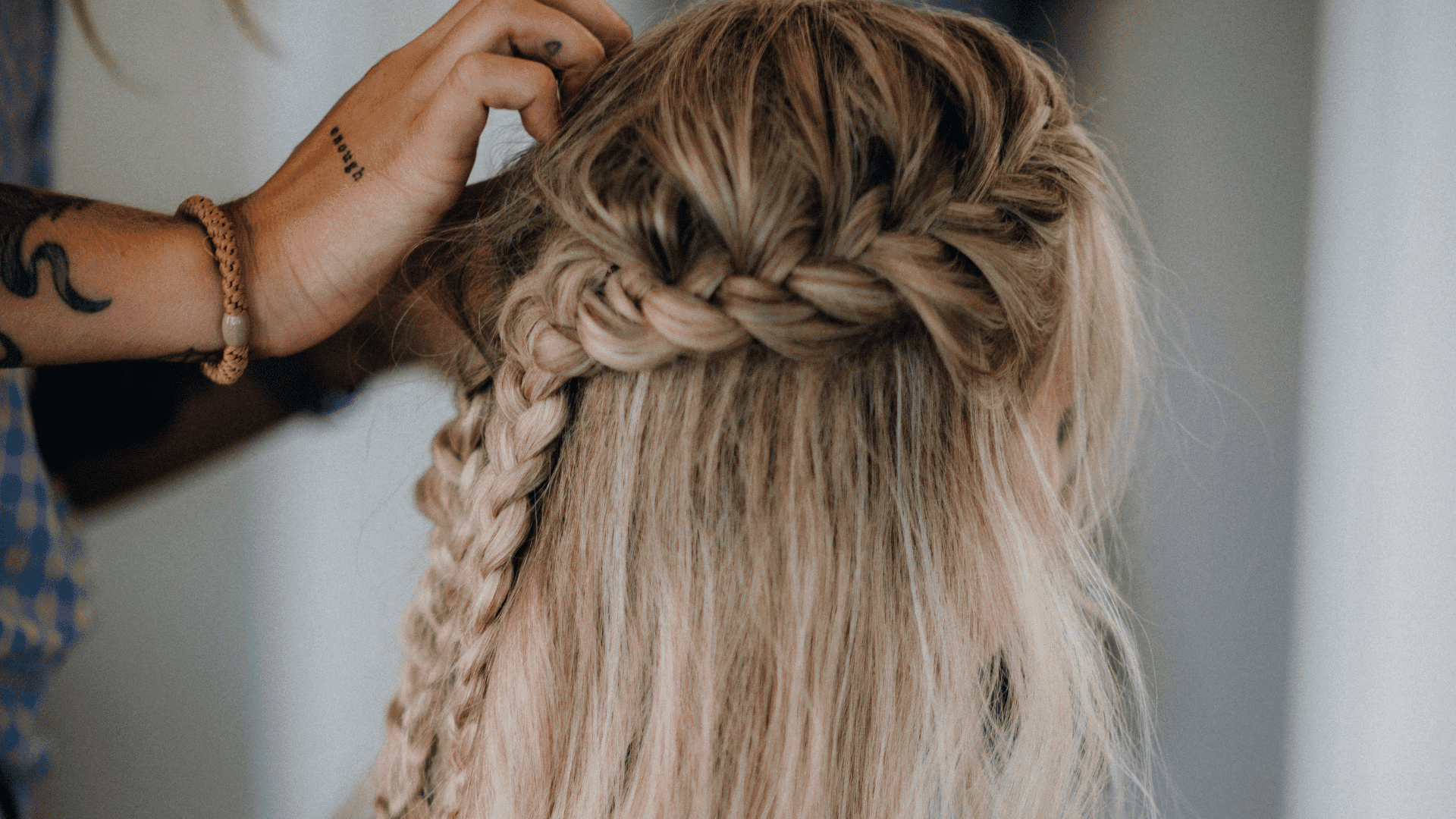 Braided hairstyle being crafted by a stylist with tattooed arms.