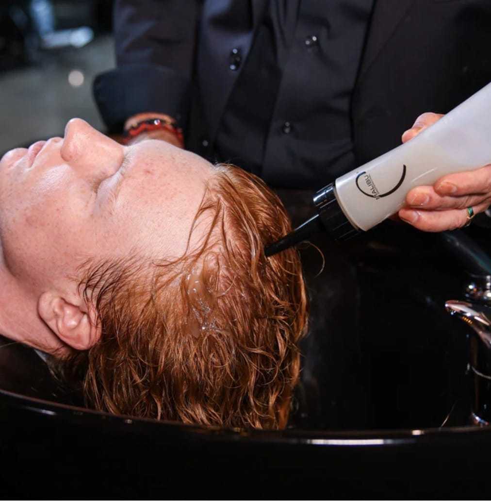 Hair stylist applying product to a person's wet hair at a salon.