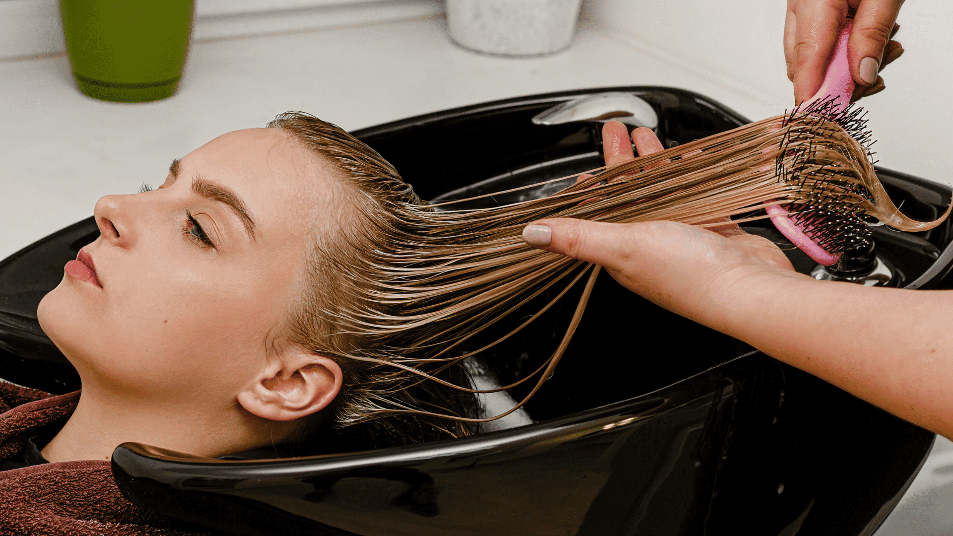 Person receiving a hair wash in a salon sink with hair being brushed.