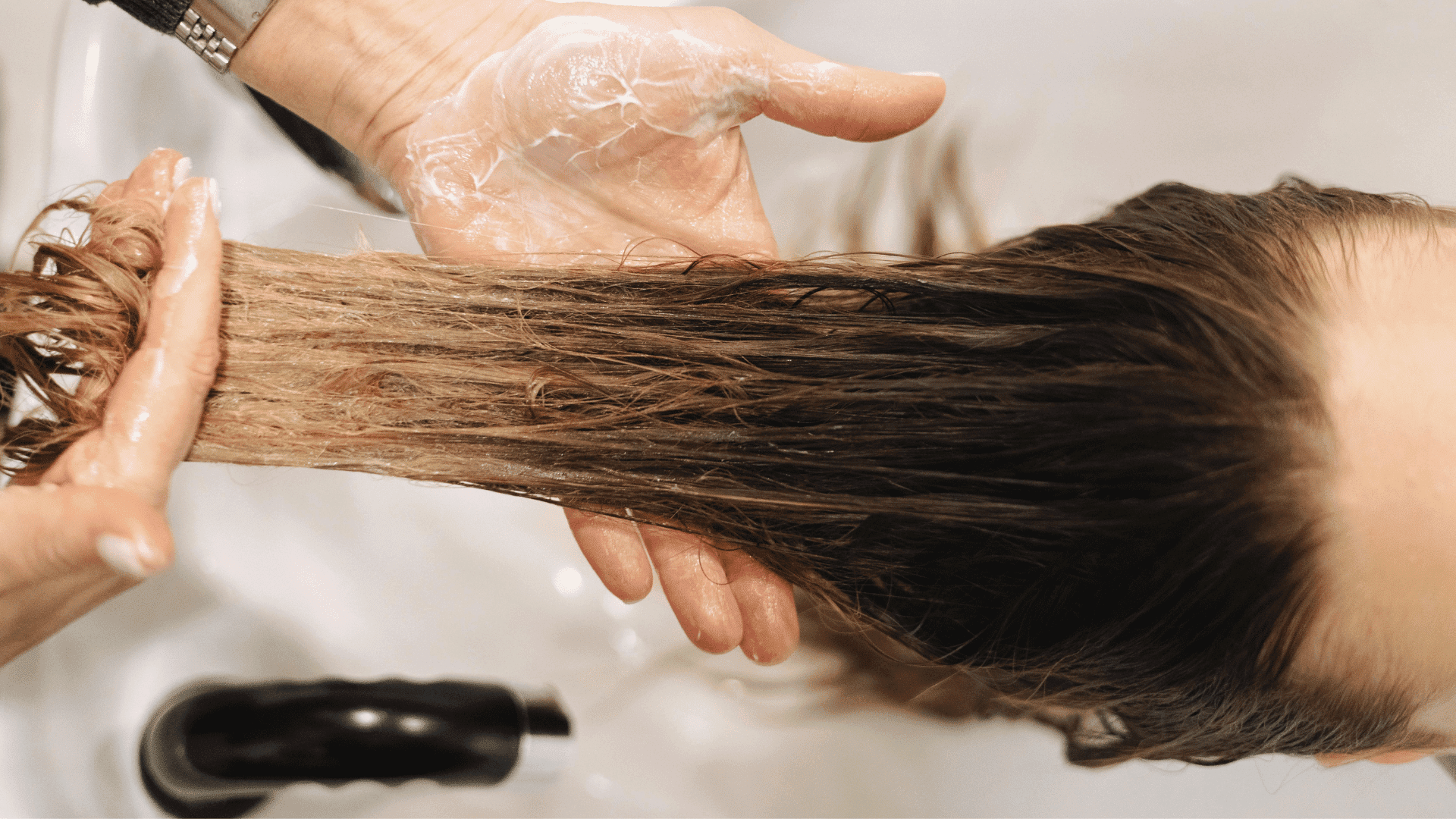Hairdresser applying conditioner to long hair in salon sink.