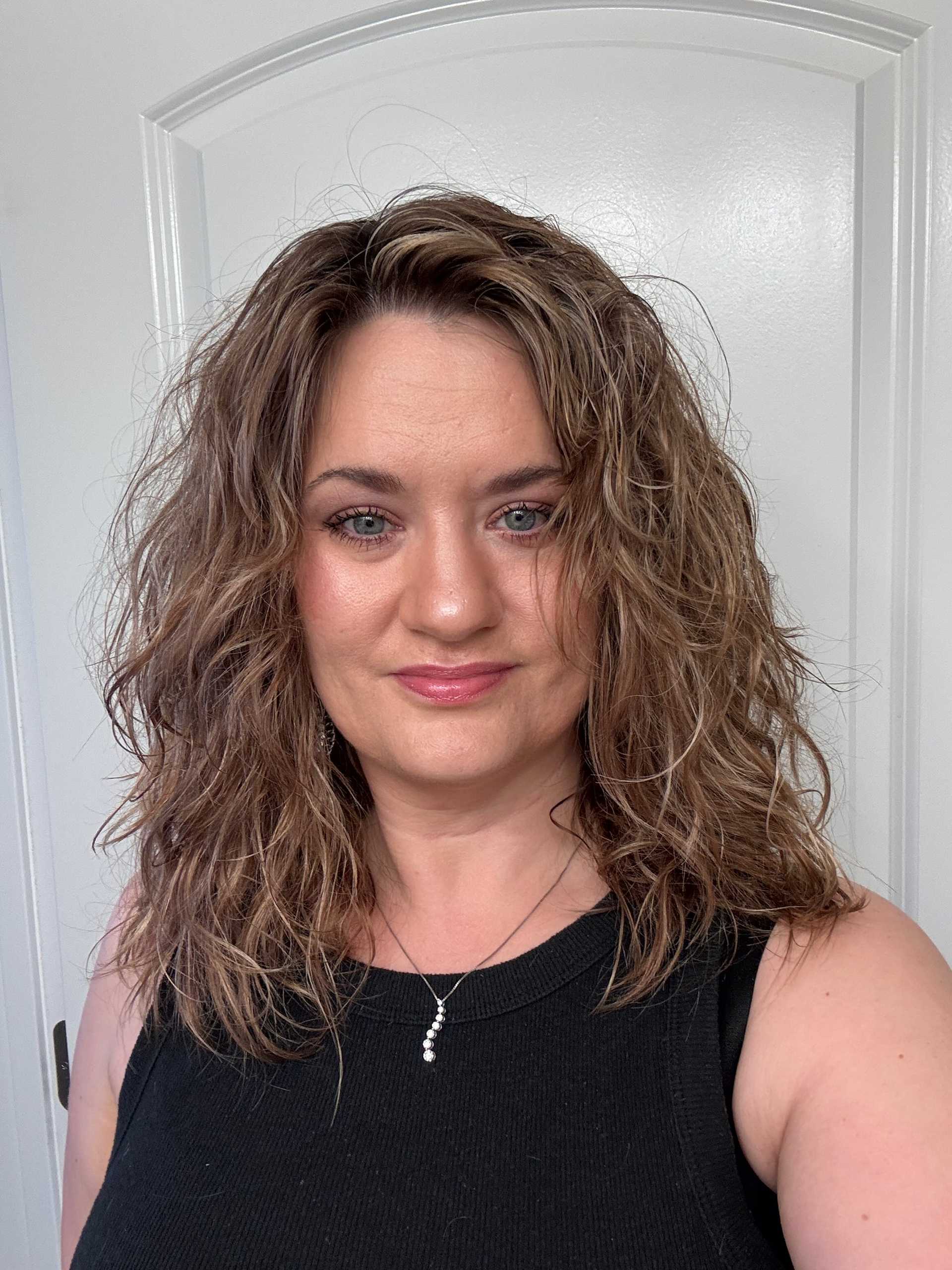 Woman with wavy hair smiling in front of a white door.