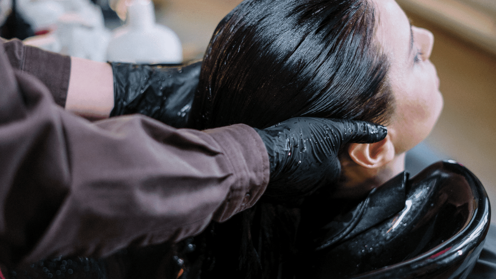 Hair salon client getting a wash with black gloves in professional hands.