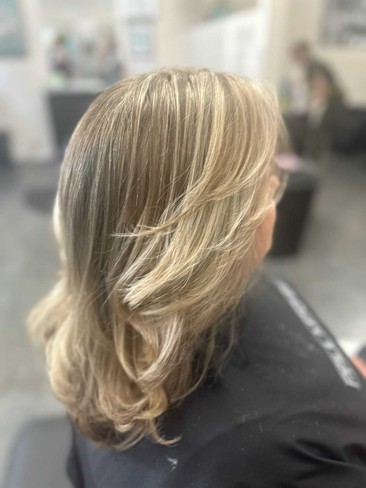 Woman with styled blonde hair, in a salon, showcasing layered highlights.