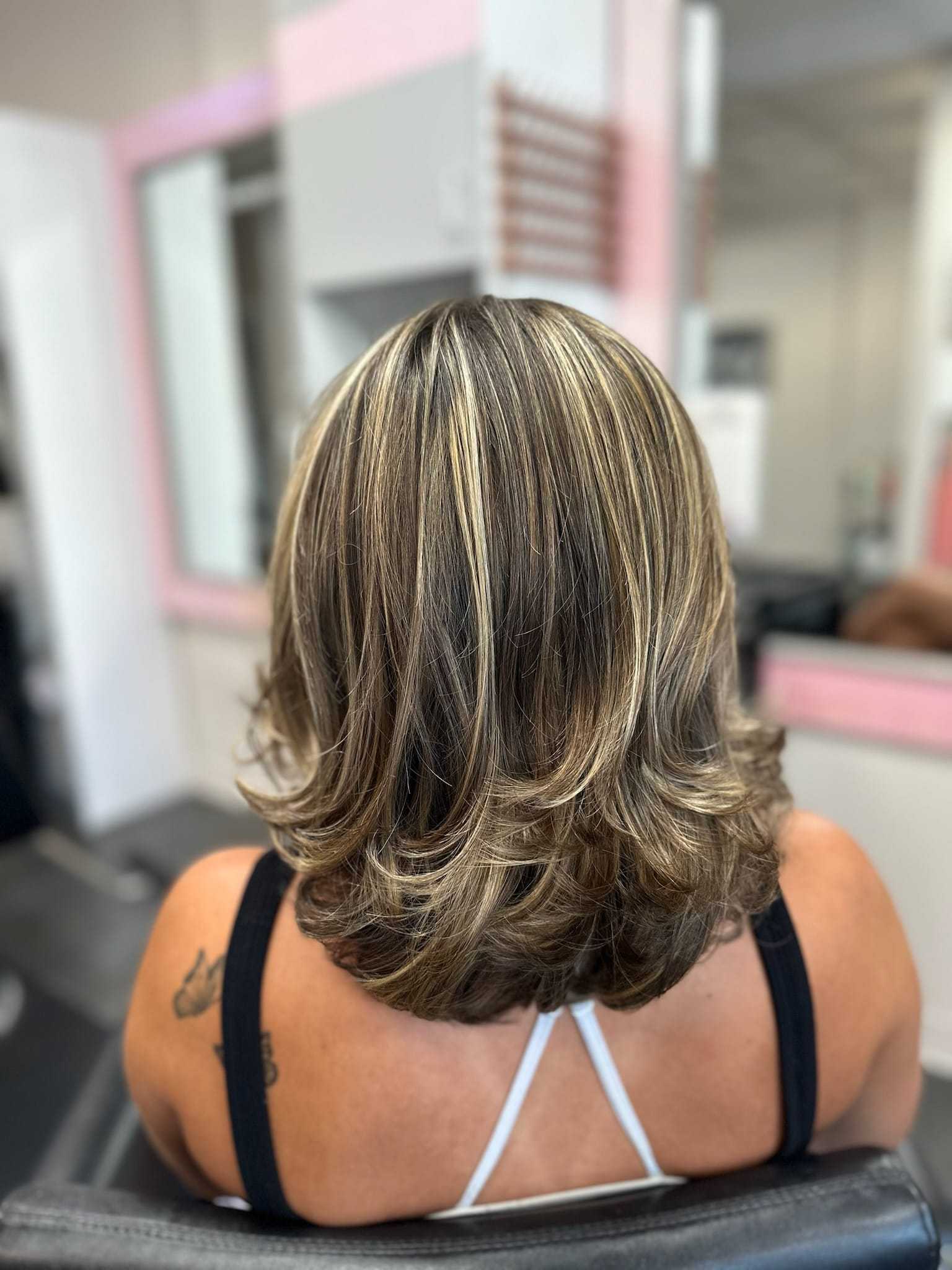Woman with layered, highlighted hair sitting in a salon chair.
