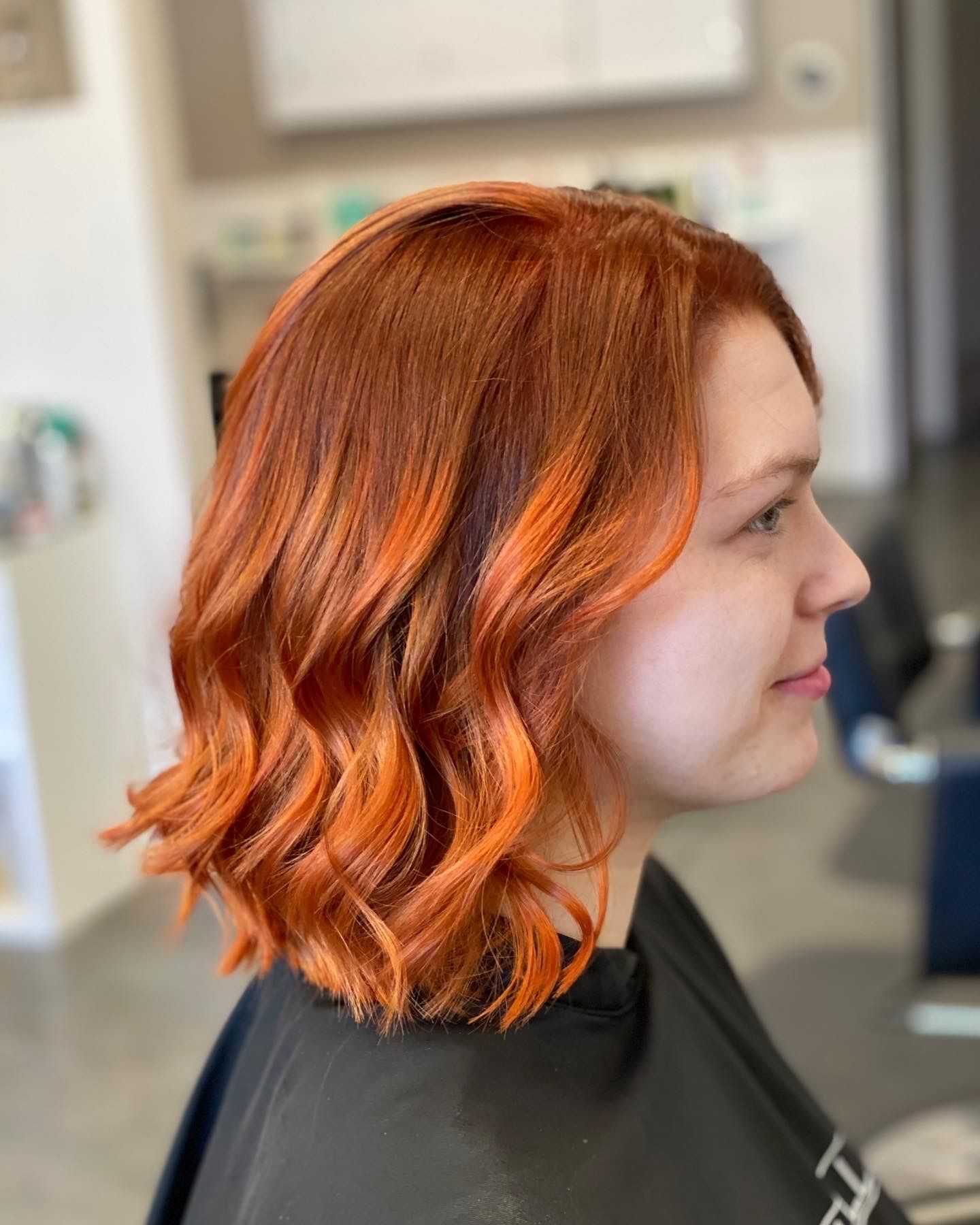 Woman with curly shoulder-length red hair in a salon chair, side profile.