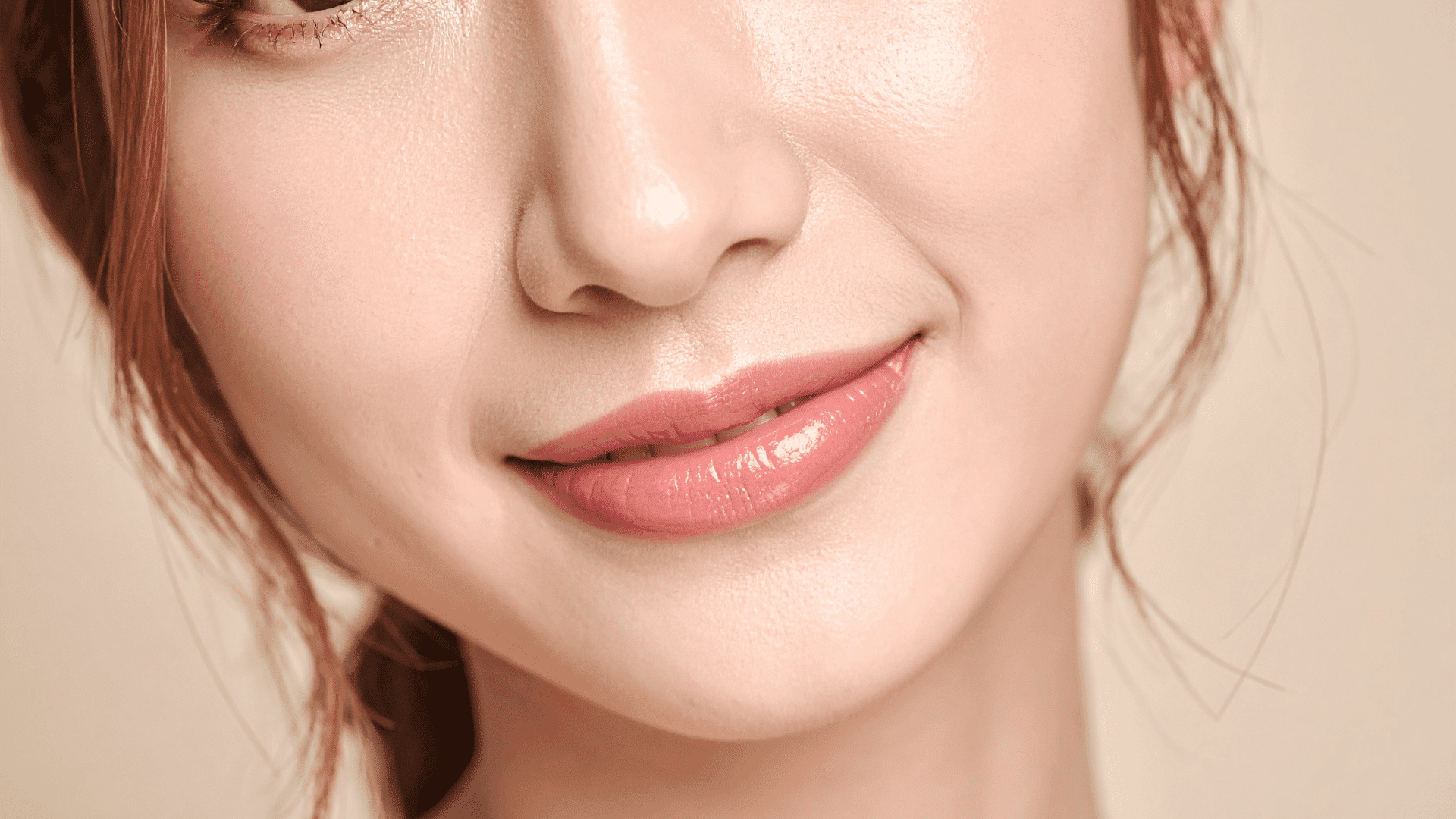 Close-up of a smiling woman’s glossy lips and smooth skin.
