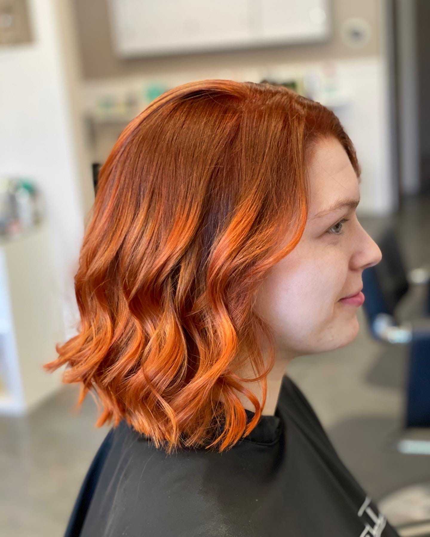 Woman with curly shoulder-length red hair in a salon chair, side profile.