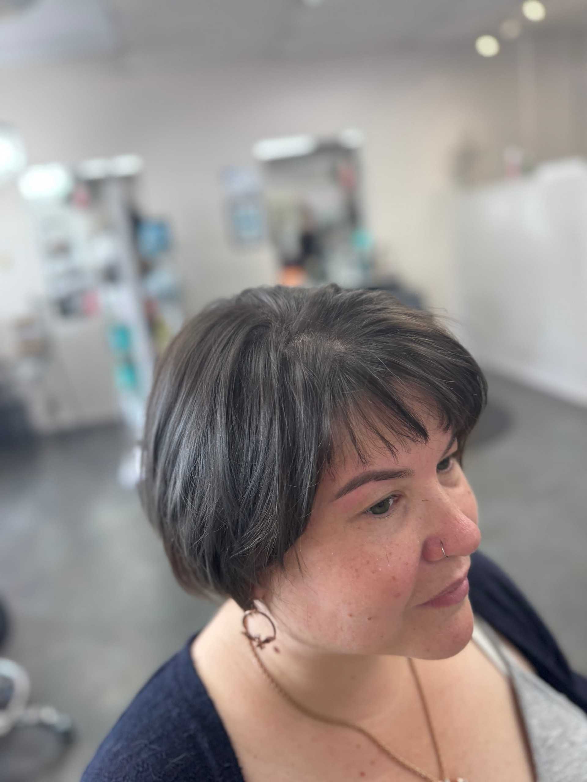Short-haired woman in a salon chair, mirrors and blurred background visible.