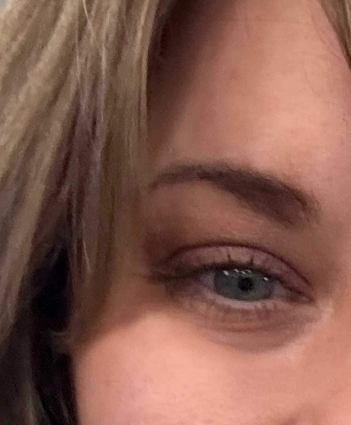 Close-up of a person's eye with brown eyelashes and light brown hair.