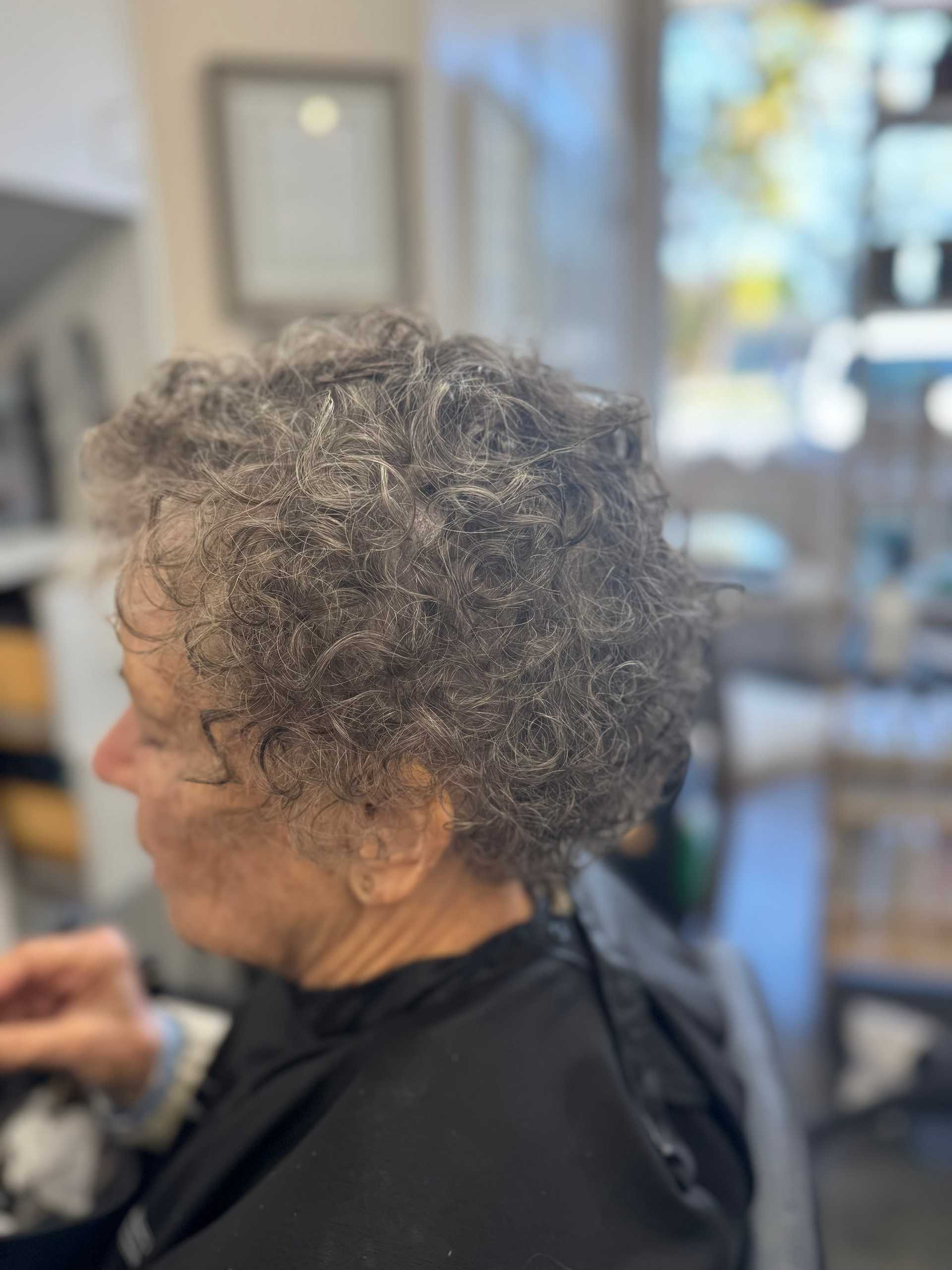 Elderly person with curly gray hair seated in a salon chair, interior view.