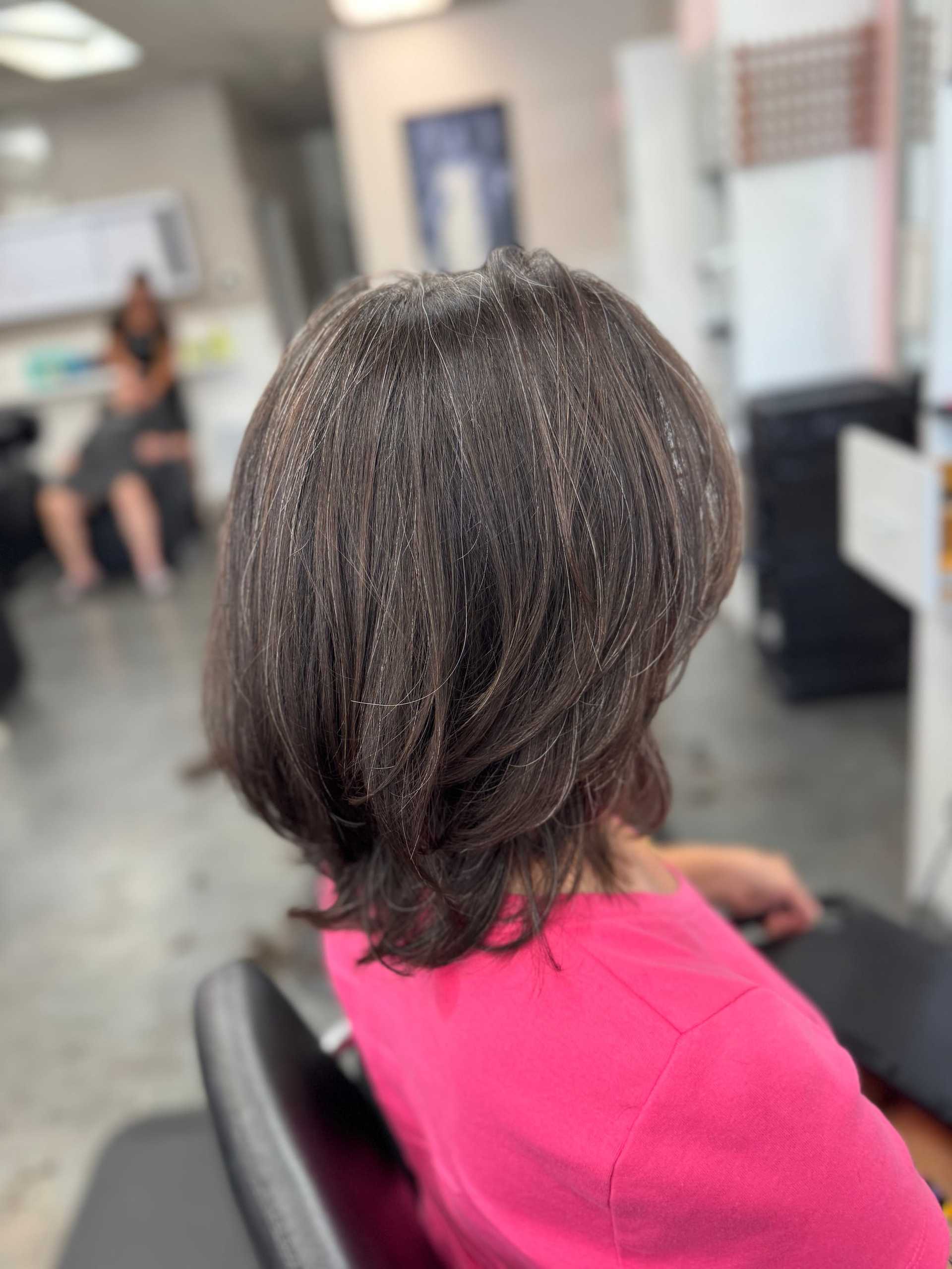 Short-haired person in a pink top sitting in a salon chair after a haircut.