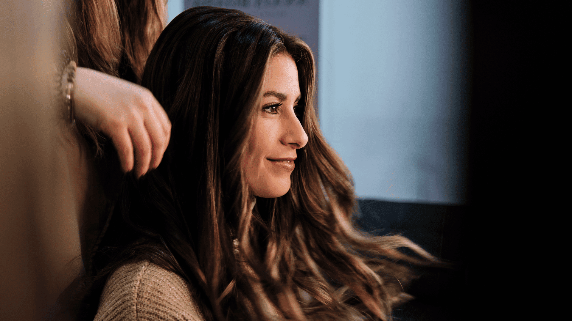 Smiling woman with long hair in salon, hand styling her hair.