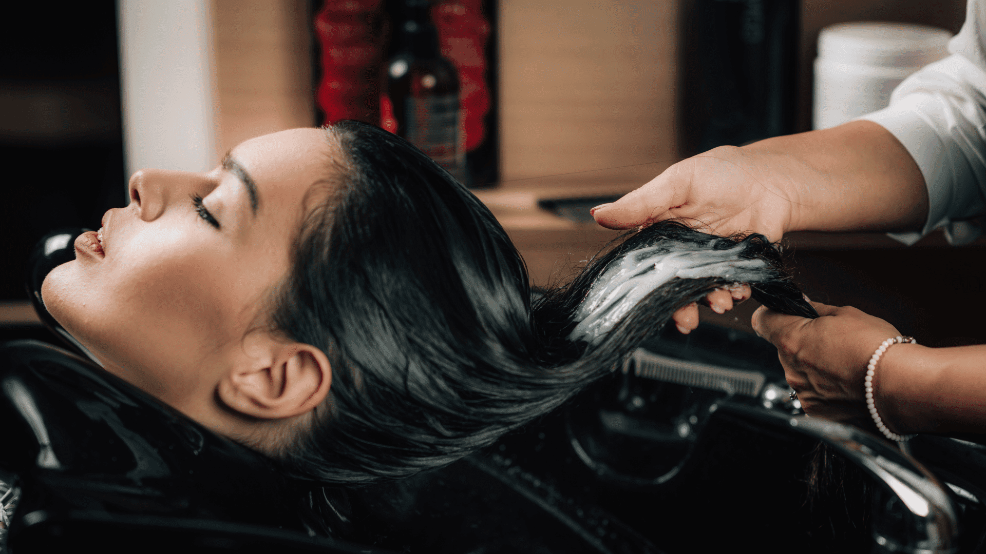 Hair salon shampooing with stylist applying lather to client's wet hair in sink.